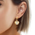 Close-up of a person wearing the Virgin Mary Flower Dangle Earrings, which are 14k gold-filled with a silver tone. The earrings showcase a captivating butterfly design with a pearl center. The person's ear and short brown hair are visible, highlighting the intricate details of these elegant earrings against the skin.